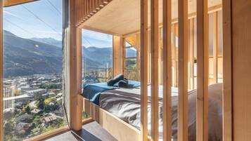 A bedroom with a bed, wooden beams, and a large window overlooking a mountainous landscape.