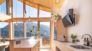 A modern kitchen with large windows, wooden cabinetry, and a view of mountains.
