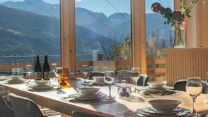 A dining table set with plates, glasses, and bottles, overlooking a mountainous landscape.