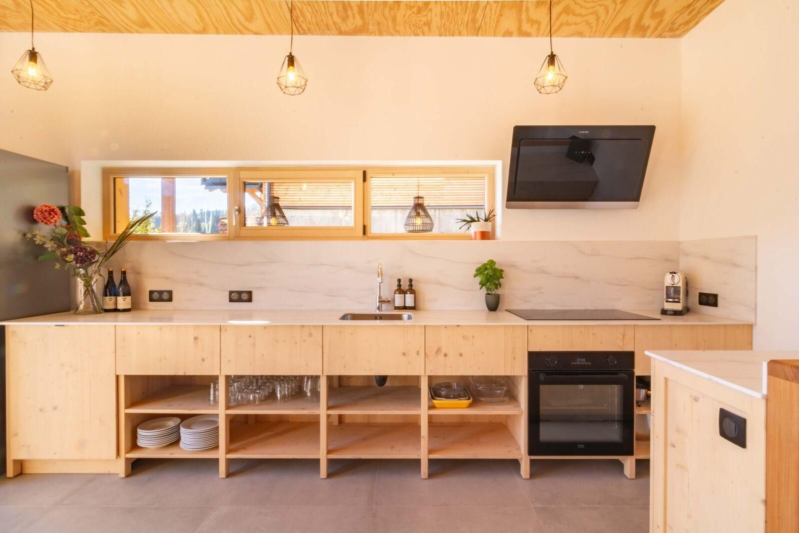 Een moderne keuken met houten kastjes, een ingebouwde oven en een groot raam met zonwering.