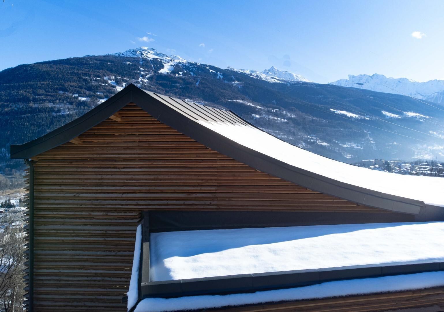 A wooden building with a sloped roof, surrounded by snow-covered mountains.