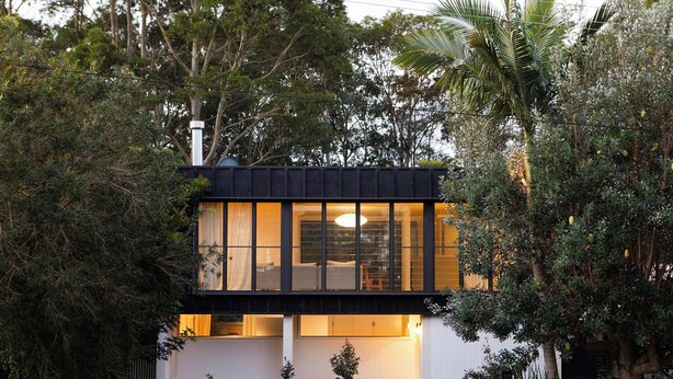 Ein modernes, zweistöckiges Haus mit großen Fenstern, einem Balkon und einem Garten.