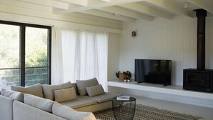 Ein modernes Wohnzimmer mit Sofa, Fernseher, Kamin und großen Fenstern.