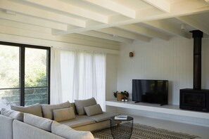 A modern living room with a sofa, TV, fireplace, and large windows. - My Malua,  Architectural Home by the Sea (Malua Bay)