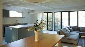Eine moderne Küche mit Kochinsel, ein Essbereich mit Holztisch und ein Wohnzimmer mit Sofa.
