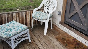 A wooden deck with a white wicker sofa and a white plastic chair with a cushion. - Tiny House on Century Farmstead (Muskego)