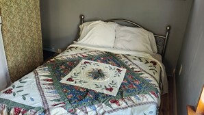 A bed with a floral quilt, a window with a view of greenery, and a radiator. - Tiny House on Century Farmstead (Muskego)