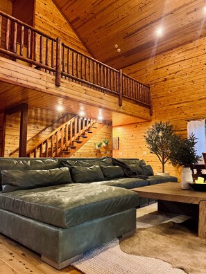 A wooden interior with a sofa, staircase, and a plant.