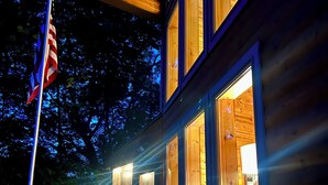 A wooden cabin with multiple windows, a deck, and an American flag. - Maxwell Reserve • Private Forest Retreat • Sleeps 14 (Tionesta)