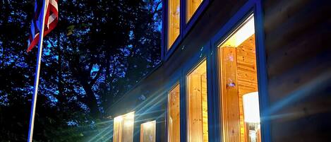 A wooden cabin with multiple windows, a deck, and an American flag.