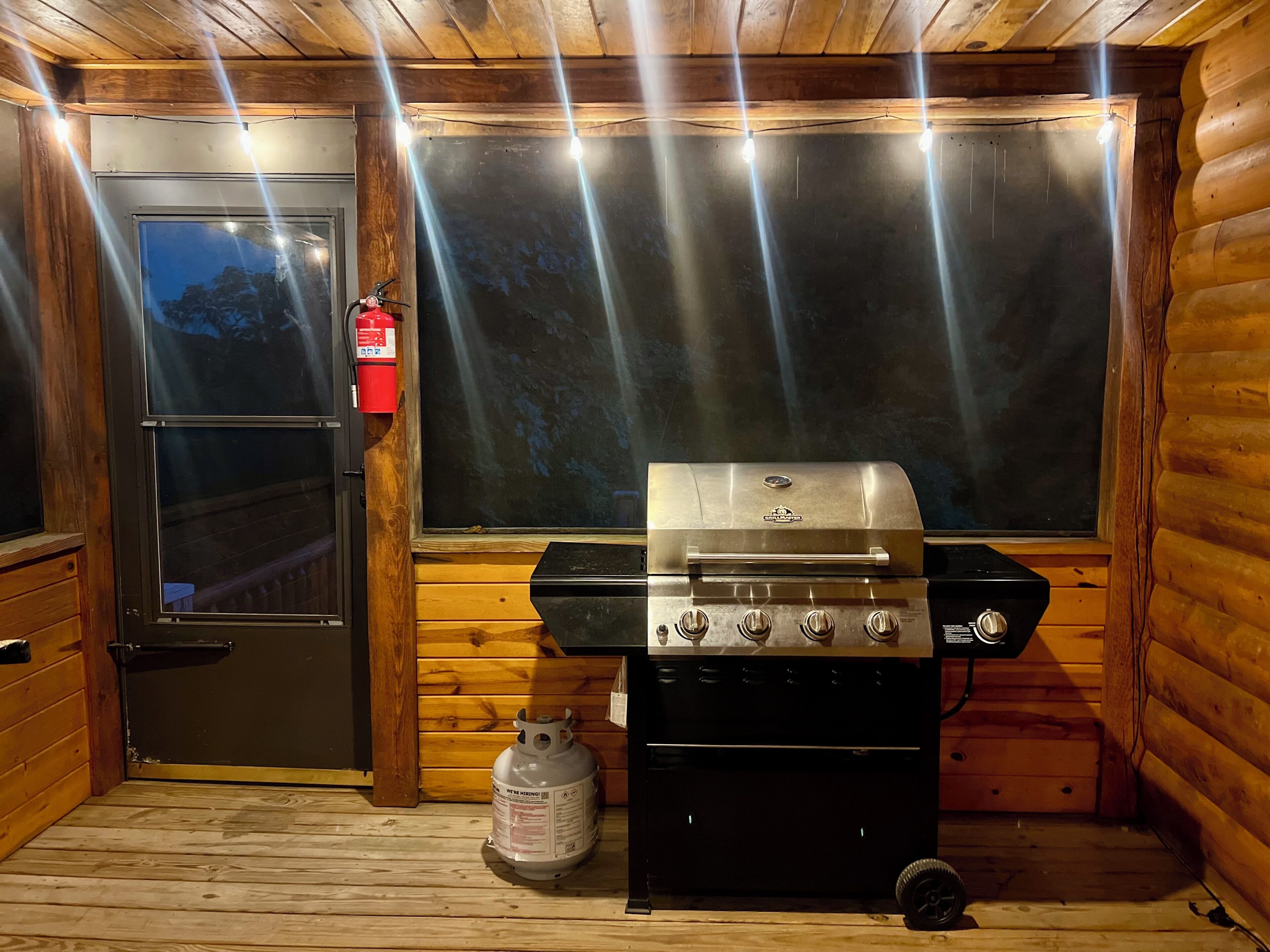Interior de una cabaña de madera con una parrilla, un tanque de propano y una puerta que contiene un extintor.