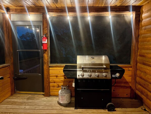 A wooden cabin interior with a grill, a propane tank, and a door with a fire extinguisher.