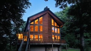 A two-story log cabin with a stone foundation, large windows, and a wooden deck. - Maxwell Reserve • Private Forest Retreat • Sleeps 14 (Tionesta)