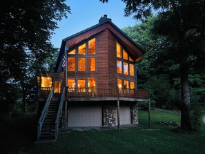 A two-story log cabin with a stone foundation, large windows, and a wooden deck. - Maxwell Reserve • Private Forest Retreat • Sleeps 14 (Tionesta)