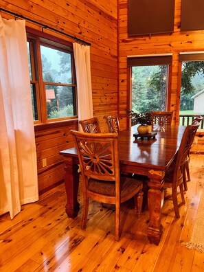 A wooden interior with a dining table, chairs, and windows.