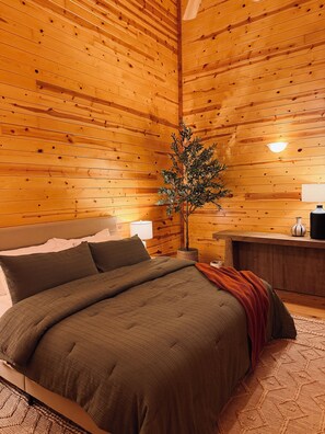 A wooden-paneled room with a bed, a nightstand, a lamp, and a potted plant. - Maxwell Reserve • Private Forest Retreat • Sleeps 14 (Tionesta)