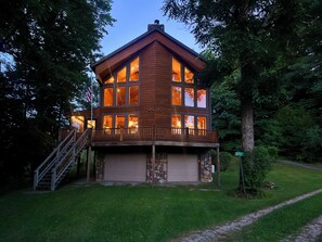 A two-story log cabin with a stone foundation, a covered front porch, and a staircase leading to the upper level.