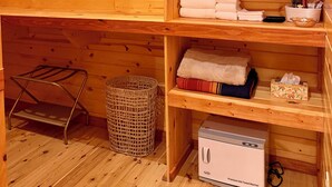 A wooden cabin interior with a built-in bench, shelves with towels, a wicker basket, and a portable heater. - Maxwell Reserve • Private Forest Retreat • Sleeps 14 (Tionesta)