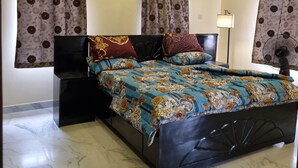 Ein Schlafzimmer mit einem Bett, Vorhängen, einer Wanduhr, einer Klimaanlage und einem Standventilator.