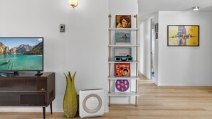 A modern living room with a flat-screen TV, a white bookshelf with various items, a decorative vase, and a white appliance. - Mile High Mid-Century Oasis, Light-Filled Central Denver Walkable Neighborhood!! (Denver)