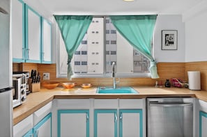 Una cocina moderna con armarios color turquesa, un lavavajillas de acero inoxidable, un fregadero y una ventana con cortinas turquesa.
