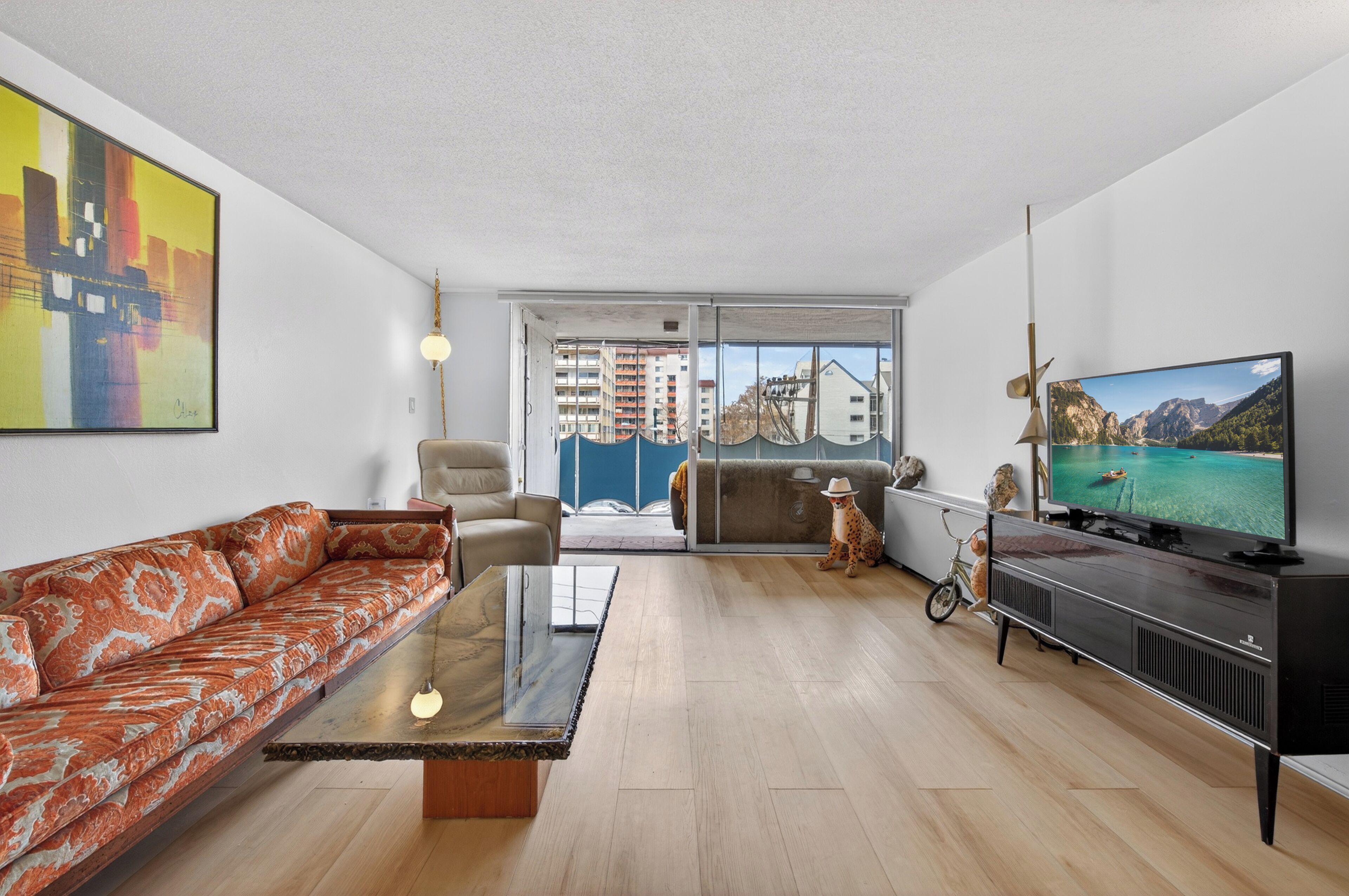 Ein modernes Wohnzimmer mit Sofa, Couchtisch, Fernseher und Blick auf eine Stadtkulisse durch große Fenster.