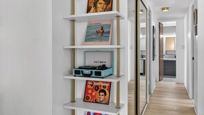 A hallway with a white wall, a shelf with vinyl records, and a door leading to a kitchen area. - Mile High Mid-Century Oasis, Light-Filled Central Denver Walkable Neighborhood!! (Denver)