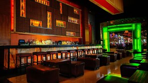 Zona bar con parete in mattoni, scaffali pieni di bottiglie e ingresso illuminato di verde.
