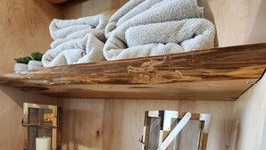 A wooden shelf with folded towels, a candle in a wooden frame, and a candle in a glass container.