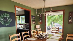 A dining room with a wooden table, chairs, a chandelier, and a view through a window.
