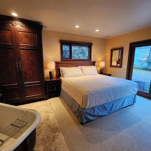 A bedroom with a large bed, a wooden wardrobe, a bathtub, and a window with blinds.