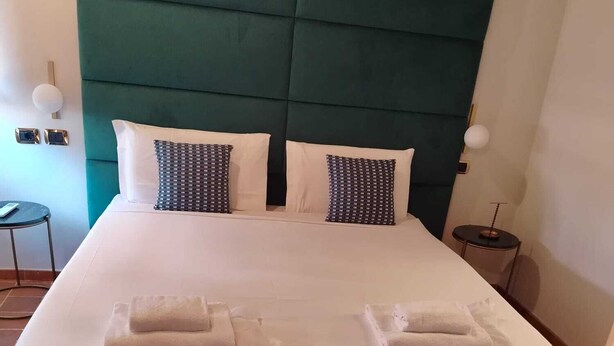 A neatly made bed with white linens and two towels, a teal upholstered headboard, and a small bedside table with a lamp. - WONDERFUL VILLA BY THE SEA (Anzio)