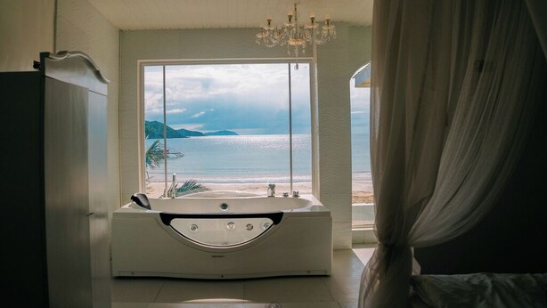 A bathroom with a bathtub, a large window with a view of the sea, and a chandelier. - Serene 8-bedroom resort with AC in beautiful El Nido (El Nido)
