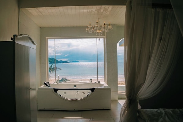 A bathroom with a bathtub, a large window with a view of the sea, and a chandelier.