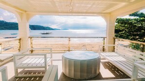 A covered outdoor seating area with a hot tub, overlooking a beach with boats and a calm sea. - Serene 8-bedroom resort with AC in beautiful El Nido (El Nido)