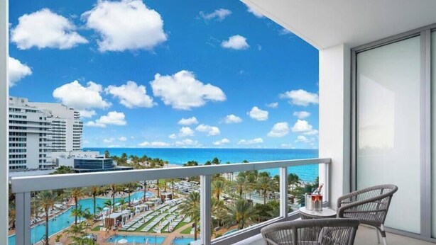 A balcony with a view of a resort pool and ocean. - Sorrento 704 (Miami Beach)