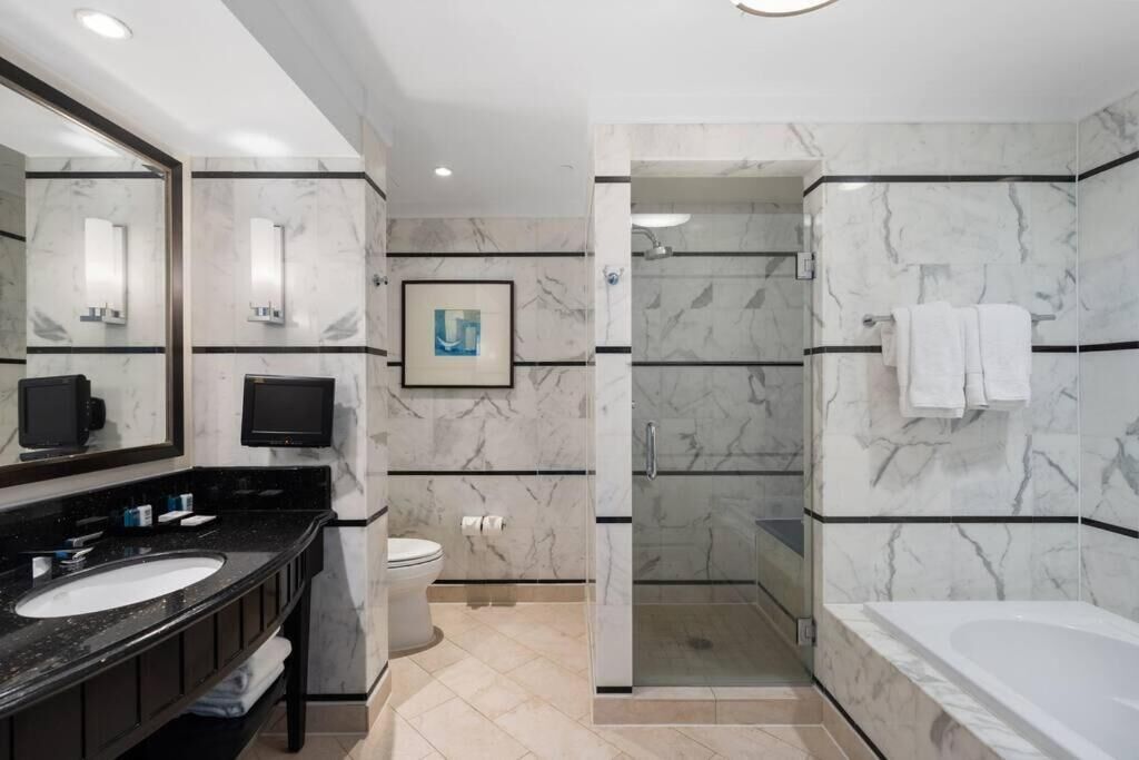 A modern bathroom with a large mirror, a sink, a toilet, a shower enclosure, and a bathtub.