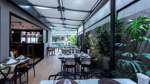Un espacio de comedor al aire libre con mesas, sillas, una barra y plantas en macetas.
