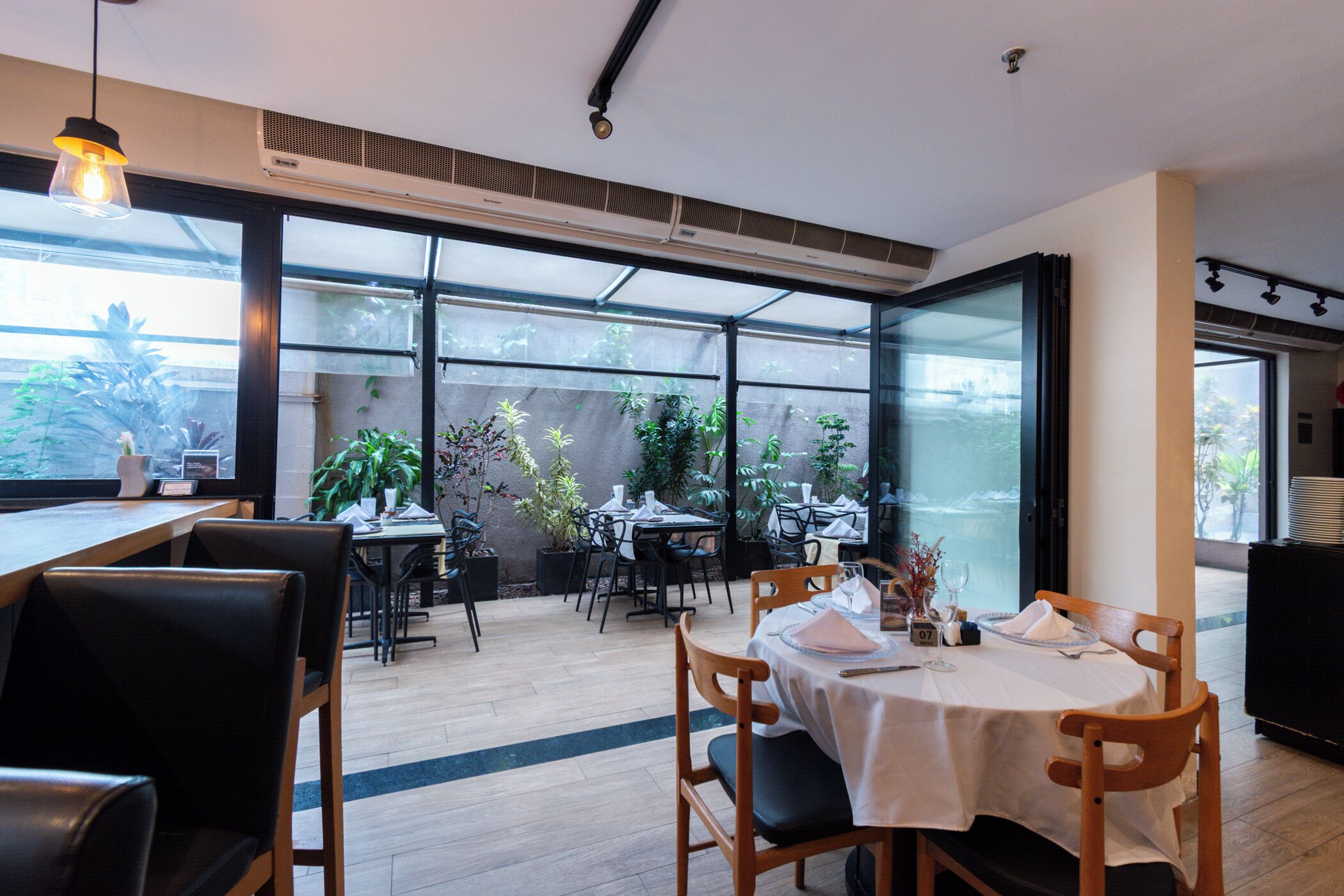 Un comedor interior con mesas y sillas, ventanas amplias y un equipo de aire acondicionado.