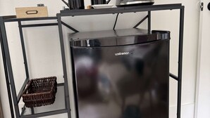 Un refrigerador negro con una cafetera encima, una cesta de mimbre y una estantería metálica negra.