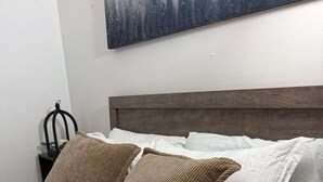 Una cama con dos almohadas marrones y sábanas blancas, un cabecero de madera y una obra de arte colgada en la pared.