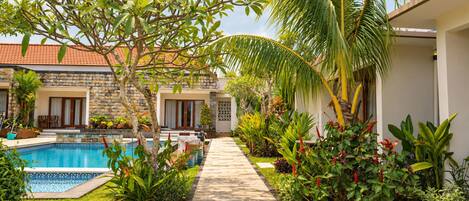 Un espace aménagé au bord de la piscine, avec un chemin bien défini, un bâtiment en pierre et une végétation luxuriante.