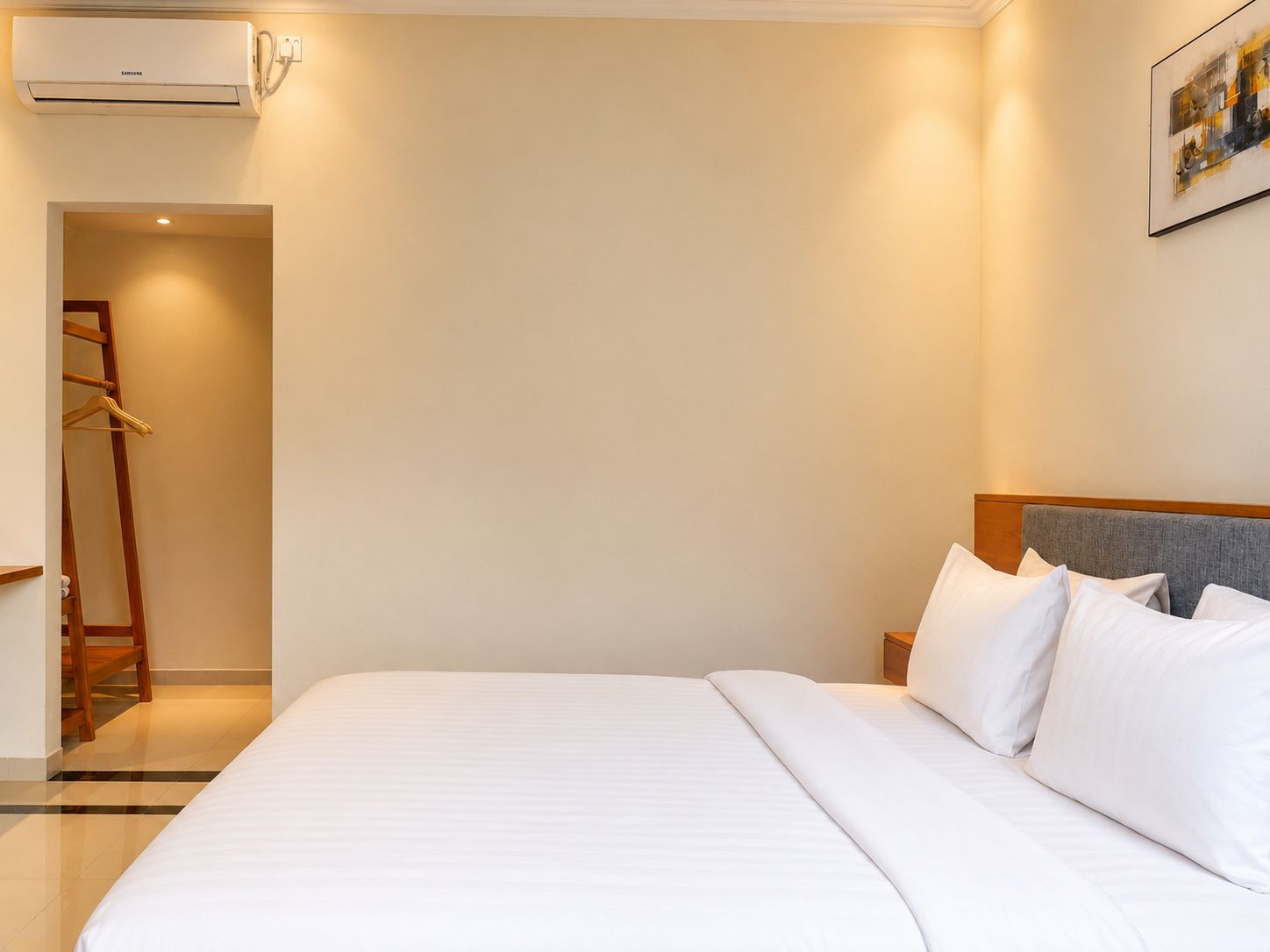 A hotel room with a bed, a nightstand, a wardrobe, and an air conditioning unit.