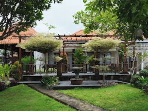 Un jardín con un pérgola, una fuente y diversas plantas.