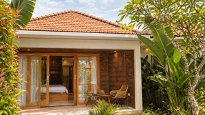 A modern house with a tiled roof, a glass door entrance, a bed, and a dining area with chairs. - d'Leisure (Kutuh)