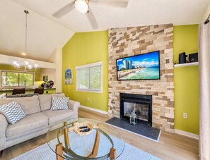 A living room with a sofa, coffee table, fireplace, TV, and a stone wall. - West Hyde Park 19D (Myrtle Beach)