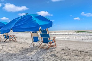 Strandstühle und Sonnenschirme an einem sandigen Strand mit dem Meer im Hintergrund.