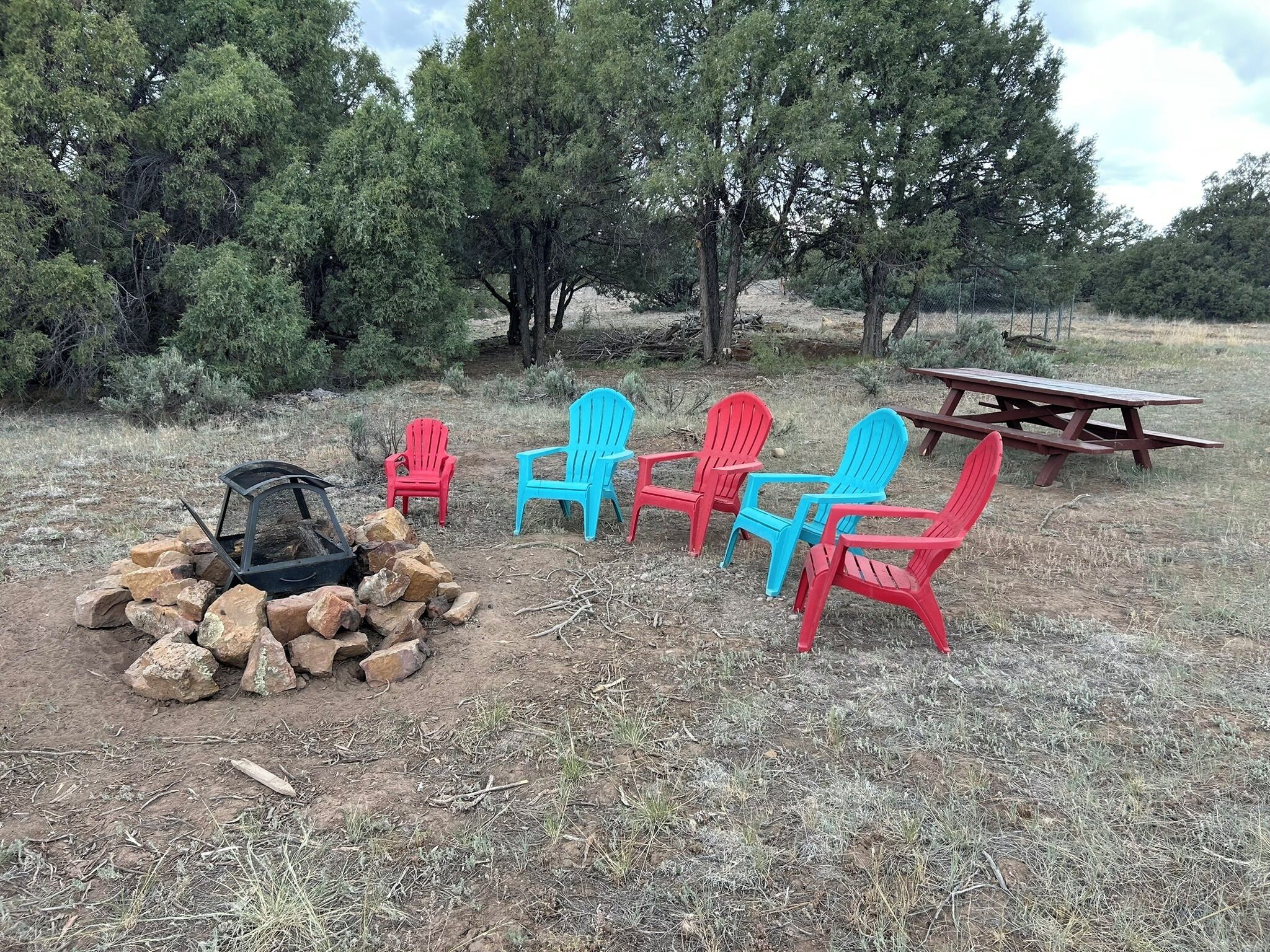 A campsite with a fire pit, picnic table, and Adirondack chairs.