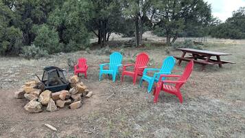 A campsite with a fire pit, picnic table, and Adirondack chairs.