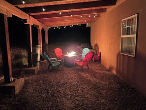 An outdoor patio with a fire pit, wooden pergola, and string lights.
